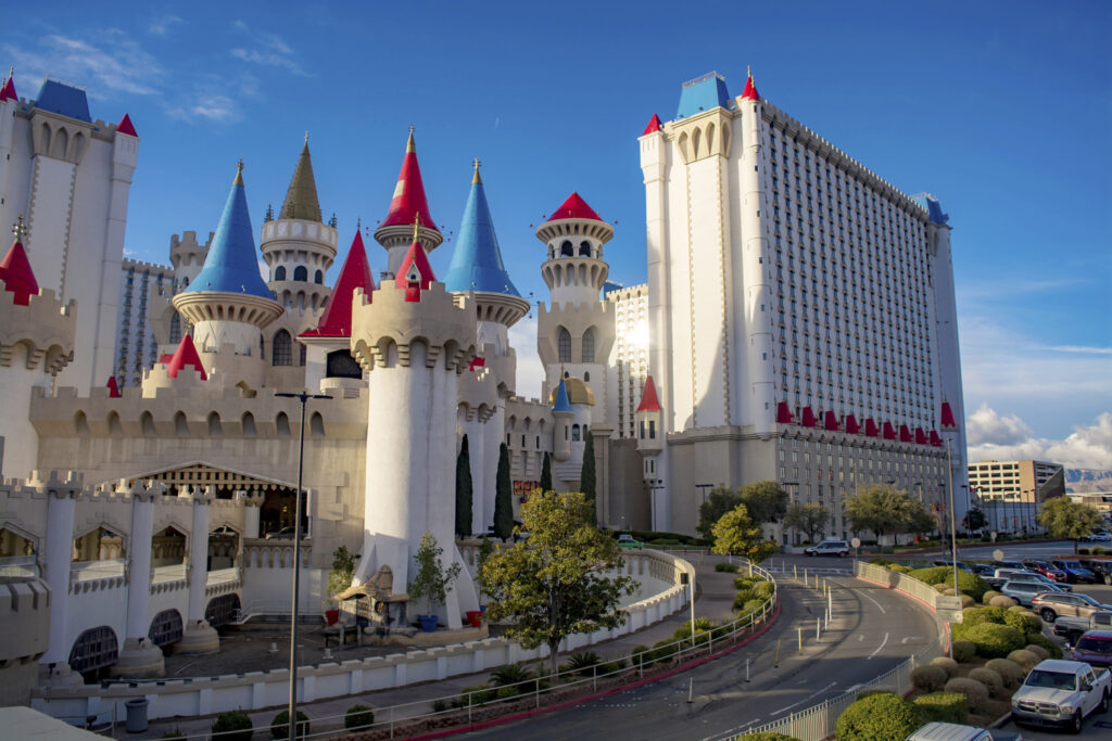 A castle-themed hotel with colorful towers and a large modern building in the background under a clear blue sky.